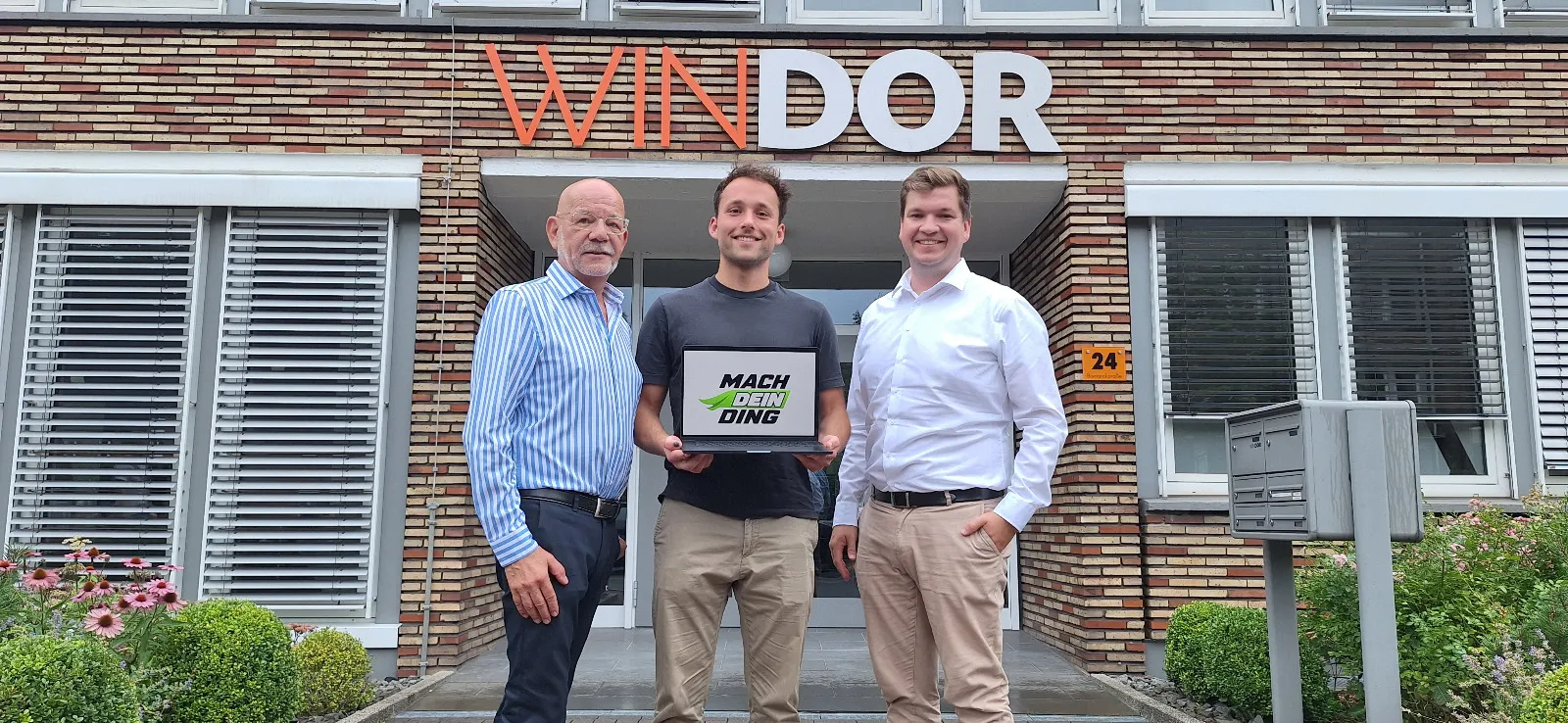 Drei Beteiligte von Mach dein Ding Dorsten vor dem WINDOR-Gebäude, mit dem Programmlogo auf einem Laptop